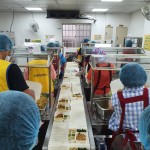 新業(yè)同仁與志工們繫上圍裙、套上防塵帽，戴上口罩，手捧一份份飯包各司其職，為的是準時將熱騰騰的飯包送到長輩手中。