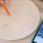 筆尖在素色瓷胚上，輕輕滑過，對(duì)照著手機(jī)上的圖樣，描繪形塑出個(gè)人獨(dú)特的風(fēng)格。